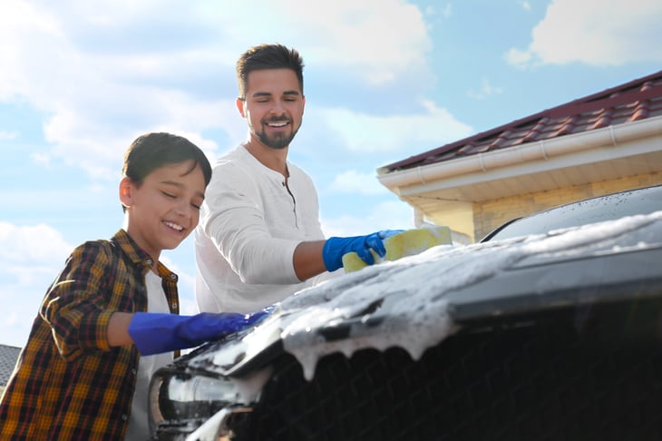 Father and son wash a car at home with sponges and soapy water.