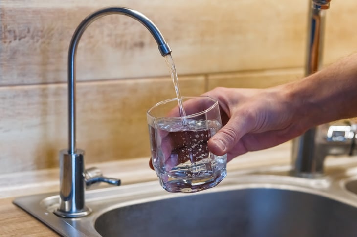 Hand holding a glass of water in front of the kitchen sink tap with a water filter