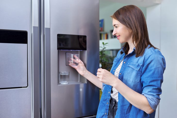 Smiling woman at home in the kitchen getting water from the fridge filtered water