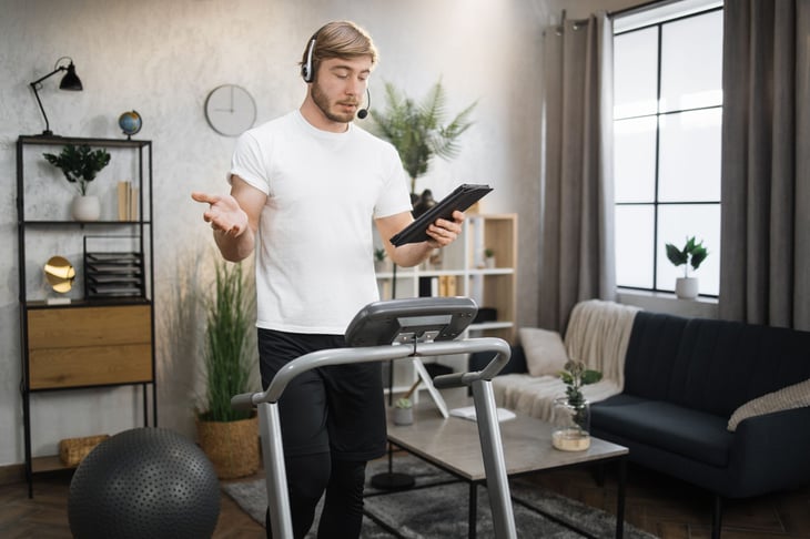 Man in headset working remotely using digital tablet, while running on treadmill.