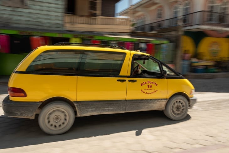 San Pedro, Ambergris Caye, Belize - November, 15, 2019. An image of a yellow taxi van driving down the cobbled street.