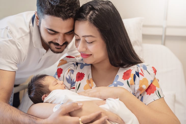 Mother and father holding a newborn baby in hospital bed.