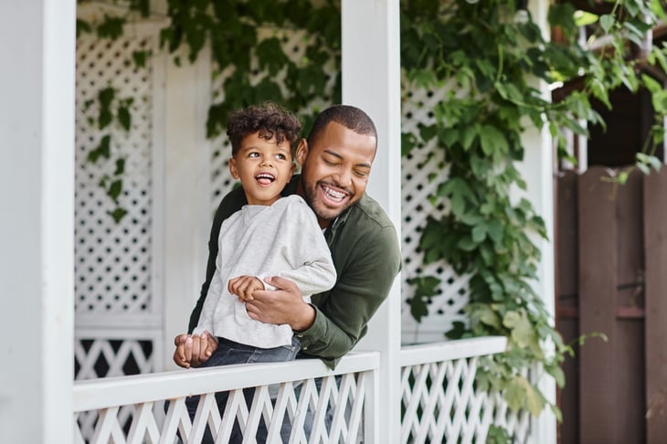 man in braces laughing and hugging son while sitting on porch