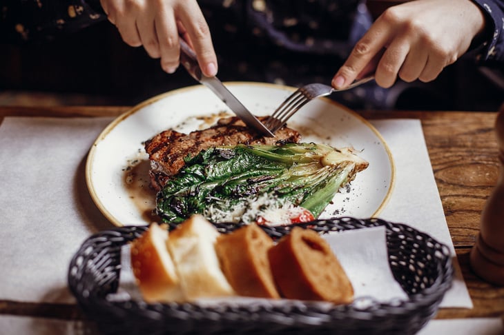 Man cutting up a steak with a knife at a dining table.