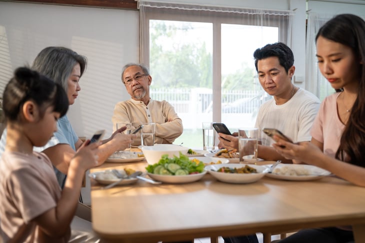 Frustrated grandfather looks at his family at the table all using phones during dinner.