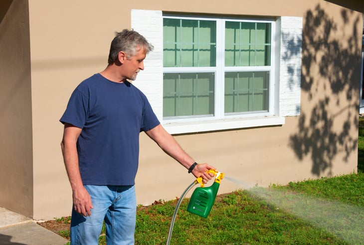 Man spraying weed killer on his front yard with a hose attachment full of chemicals that kills weeds and fertilizes the grass.