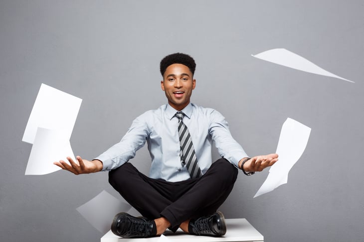 Man sitting on copier while paper flies everywhere.