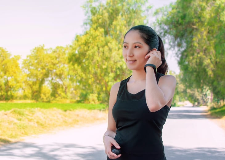A woman adjusting her hearing aid while outside.