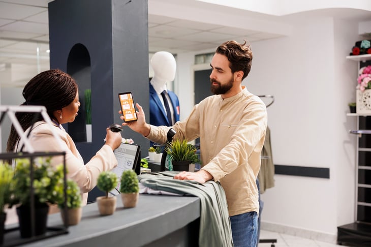 Cashier scans a digital coupon on a man's phone at a department store.