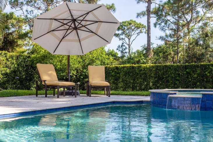 A backyard pool with chairs and an umbrella.