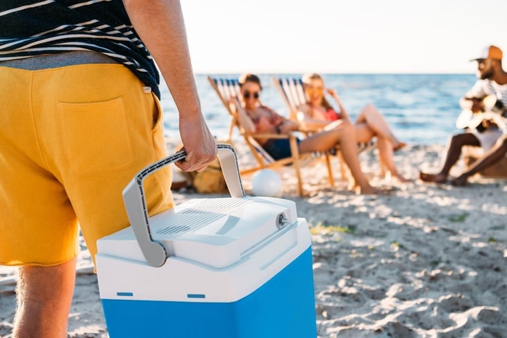 Man brings cooler over to group of friends at the beach.