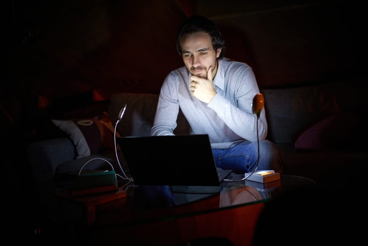 Man sitting in the dark working on a laptop with a bright screen at night
