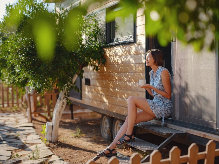 A woman drinking coffee in the morning in front of tiny home.