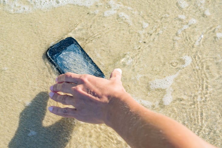 person picking up cellphone out of water on beach