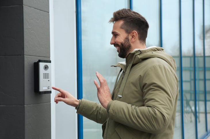 Man waves at video doorbell ringing the button to enter his apartment building or home
