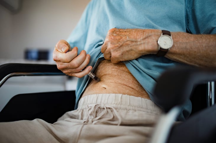 Diabetic senior patient in a wheelchair injecting insulin in his abdomen.