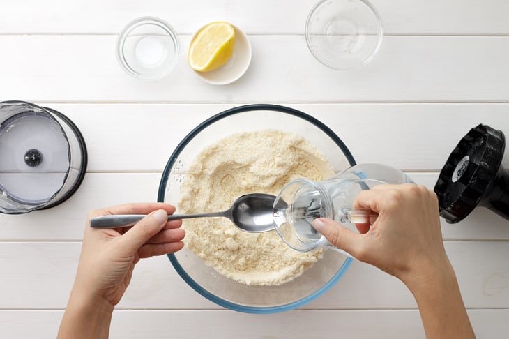 hands pour water from a jug into a bowl of flour.