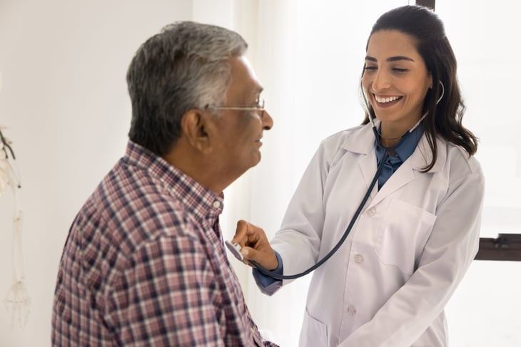 Cardiologist listening to an older male patient's heart with a stethoscope.