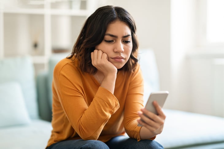 Bored, frustrated, or sad woman looking at smartphone impatiently or upset