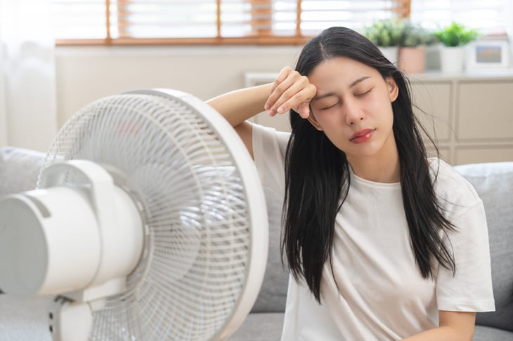 Young woman sits in front of a fan inside during a heat wave.