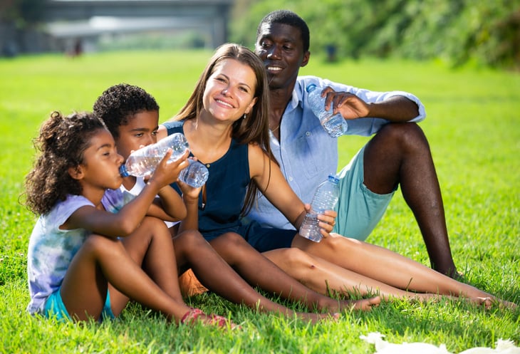 family sitting on green lawn, relaxing and drinking water