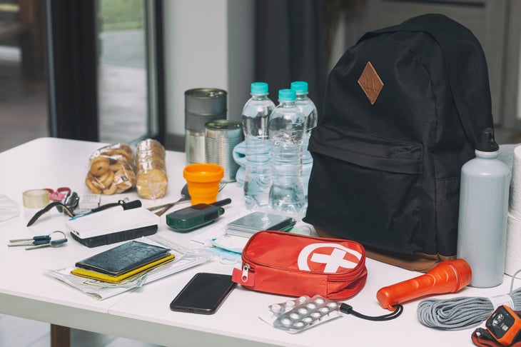 Emergency supplies on a table. Documents, water, food, first aid kit and other items needed to survive.
