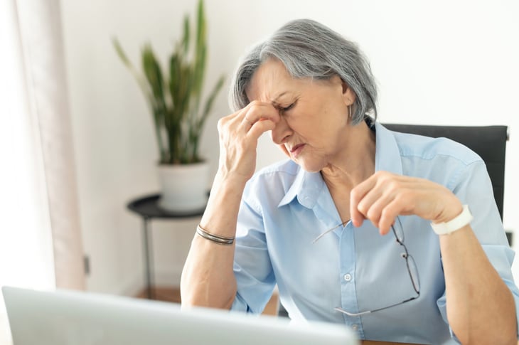 Retired woman shocked by expenses that give her a headache as she looks at her laptop.