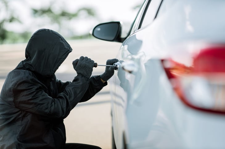 Man dressed in black holding screwdriver to break lock and steal a vehicle on the road