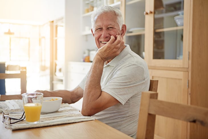Smiling older man at a table at home with cereal and orange juice.