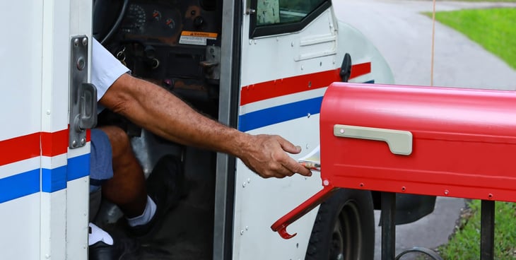 Mailman putting envelope in mailbox.