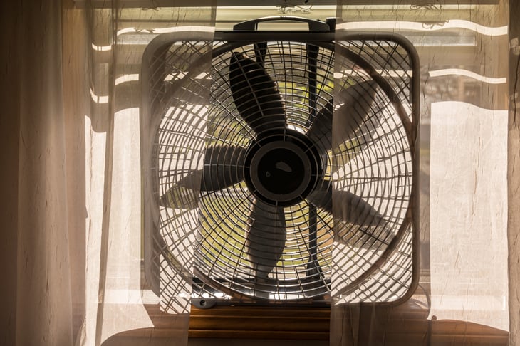 Electric Box Fan Sitting on a Window Sill with Sheer Lace Curtains.