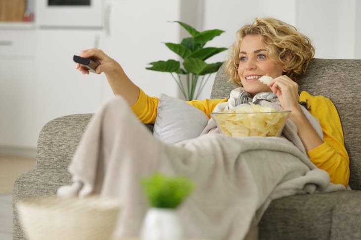 woman with bowl of potato chips watching tv on sofa