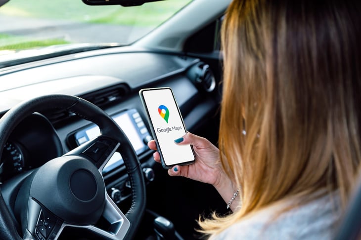 Woman in a car looking her phone with Google Maps on the screen.