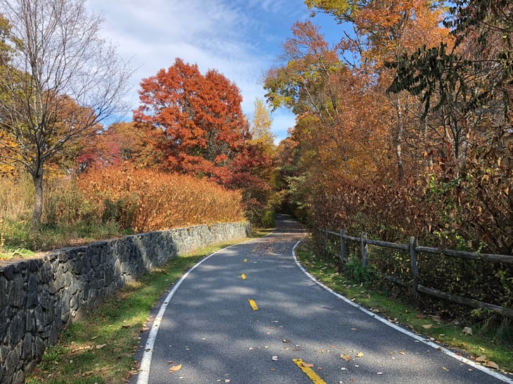 Brilliant fall foliage, bike trail, and stone wall on Ten Mile River Greenway in Pawtucket, Rhode Island