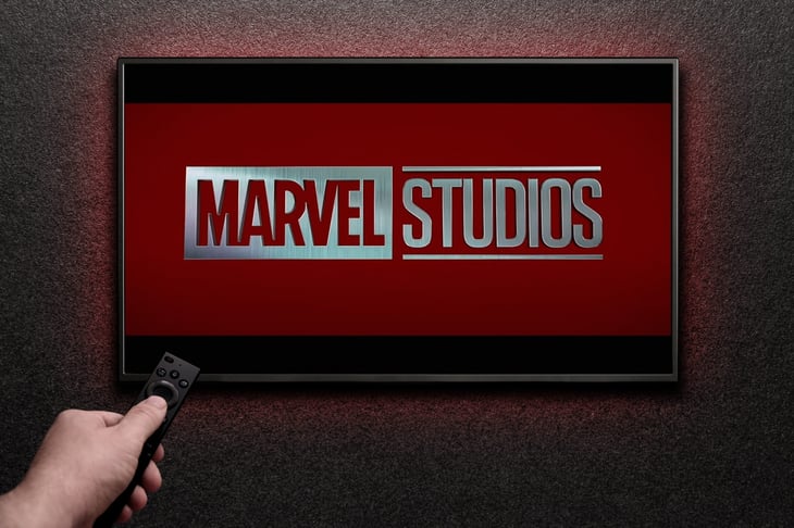 Man turns on TV with remote control. TV screen playing Marvel Studios movie.