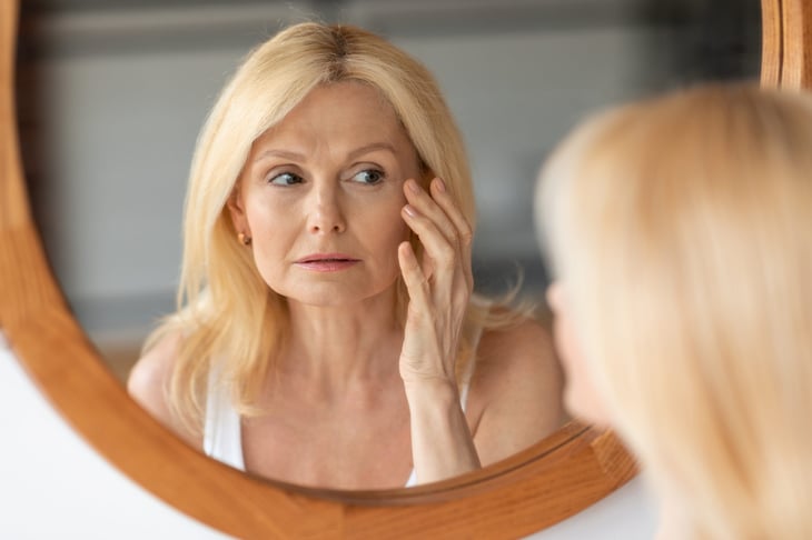 Woman touching her face while looking in the mirror