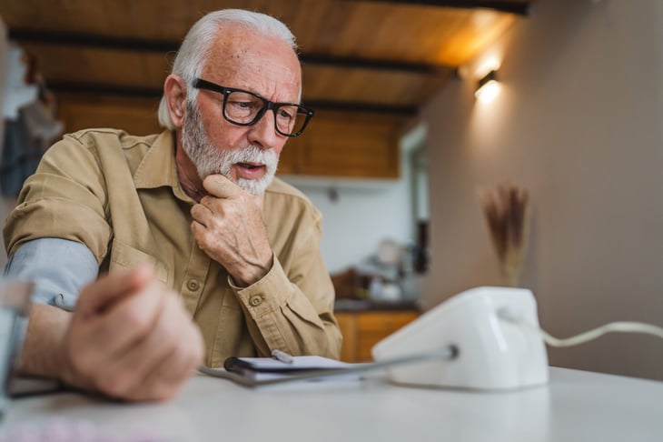 Older man at home taking blood pressure, looking concerned about the results.