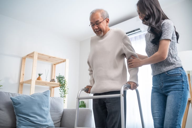 Young woman helps her senior father with his walker at home.