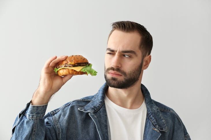 Man looking a hamburger suspiciously