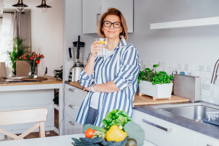 older woman in kitchen drinking water and making a salad
