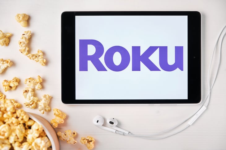 Roku logo on a tablet screen on a table with scattered popcorn and Apple earphones.