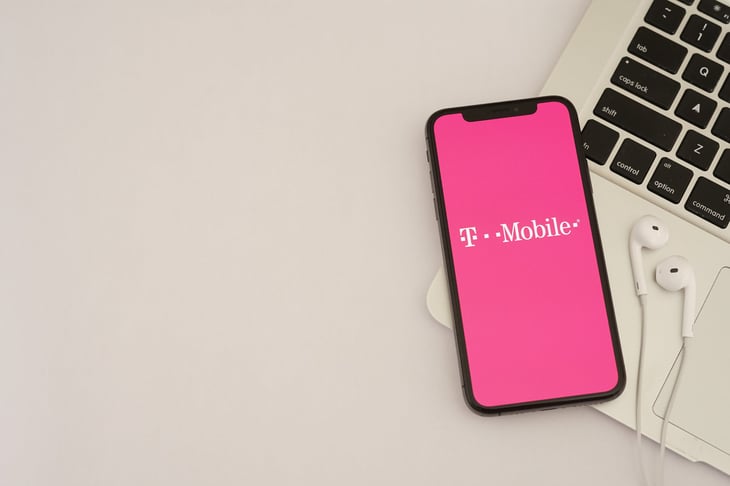 T-Mobile app on a smartphone with a Macbook and earphones.