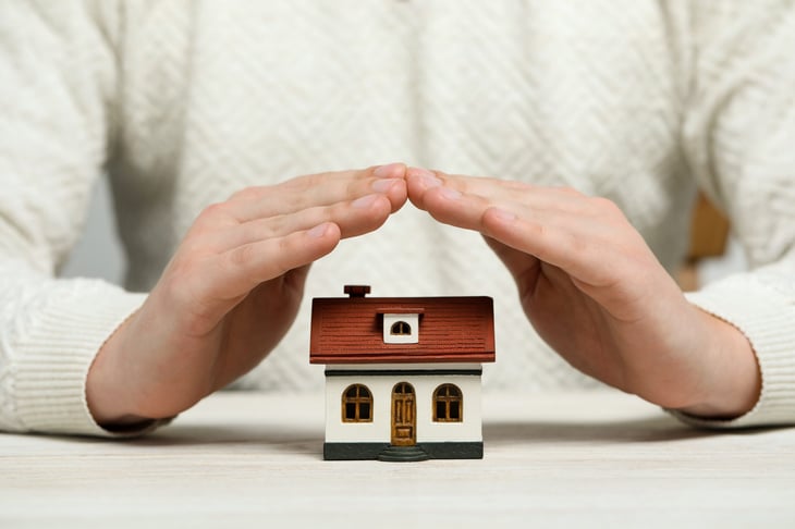 Hands over a toy house, symbolic of protection and security