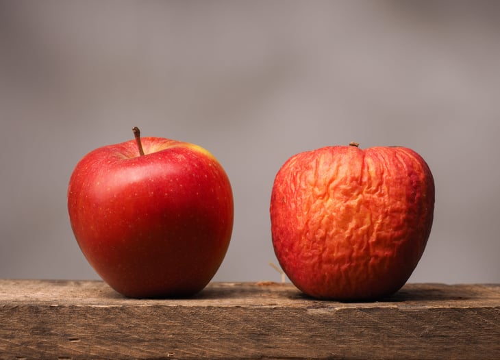 Two red apples on a rustic wooden table, one fresh and one spoiling