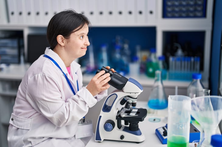 Young woman scientist with down syndrome smiling and using a microscope in a laboratory