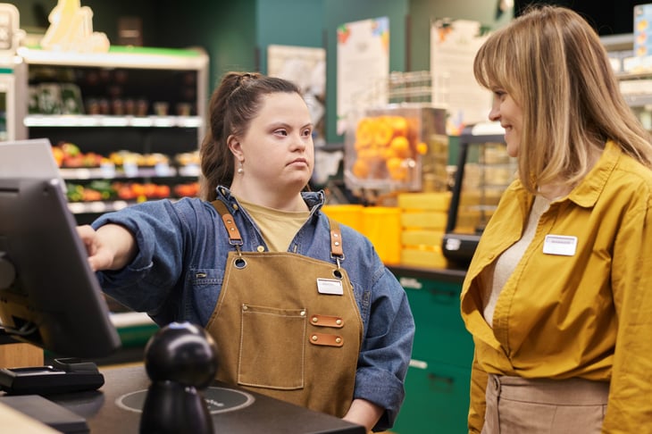 young woman with disability working at cash register in supermarket with manager