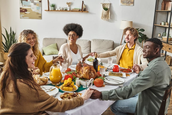 A family sitting at festive table holding hands cheerfully on Thanksgiving.