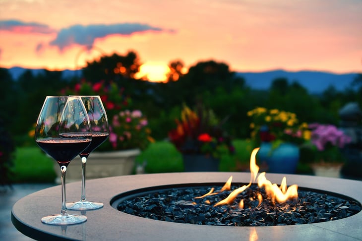 Two glasses of red wine next to an outdoor fire at sunset