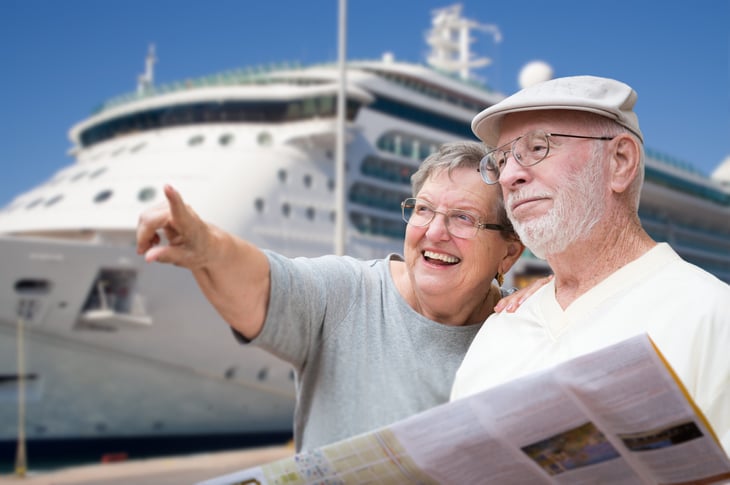 Smiling retirees next to a cruise ship holding a map and pointing