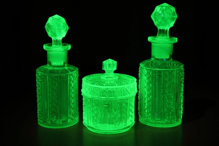 Art deco molded green uranium glass lit by UV light on a table. The uranium glows green with fluorescence.